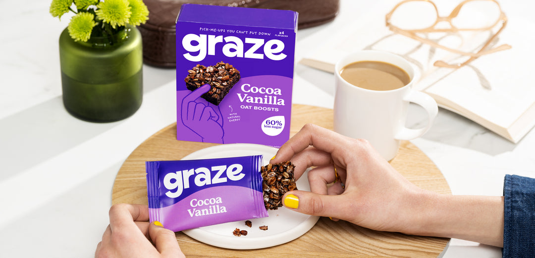 Graze cocoa vanilla oat boosts being opened next to a cup of tea and plant