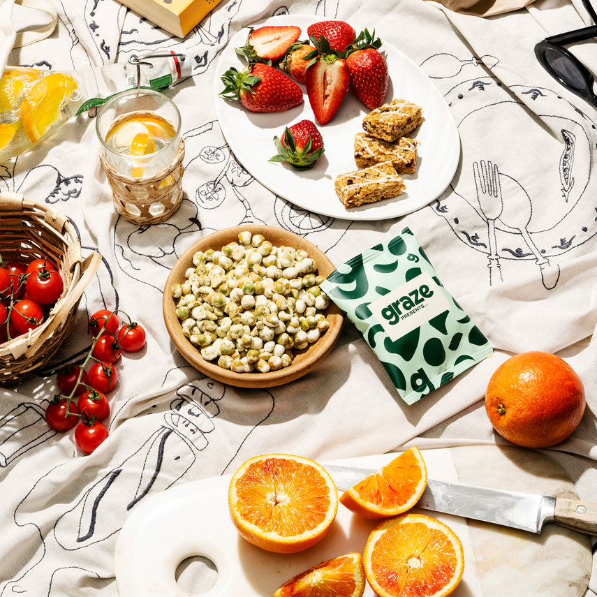 The contents of the 'a garden in bloom box' on a picnic rug with fruits, oranges, tomatoes and strawberries