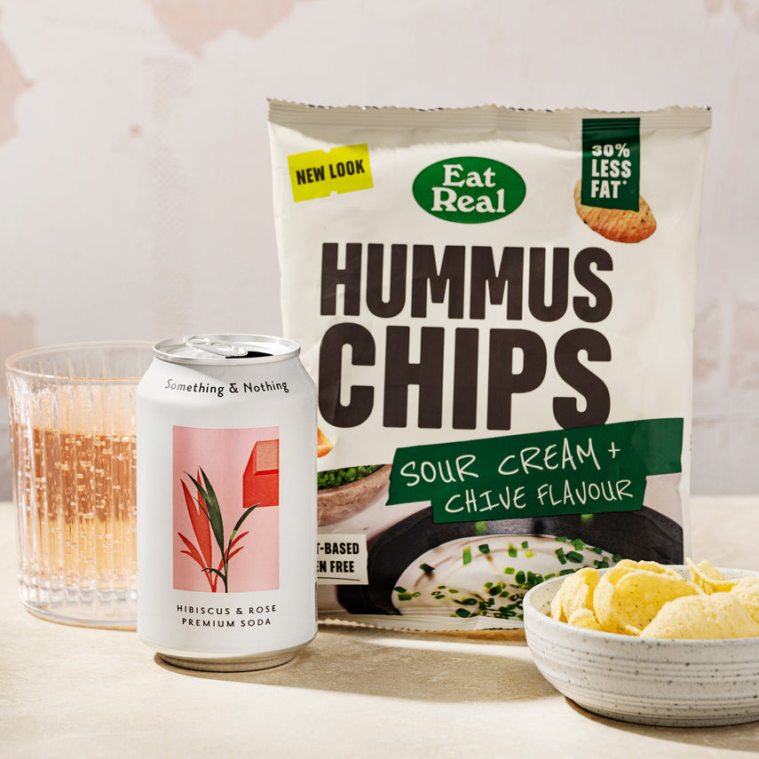 The partner products in the Graze 'a garden in bloom box'. Something & Nothing pink hibiscus & rose premium soda sparkling in a clear glass and hummus chips in a small white bowl