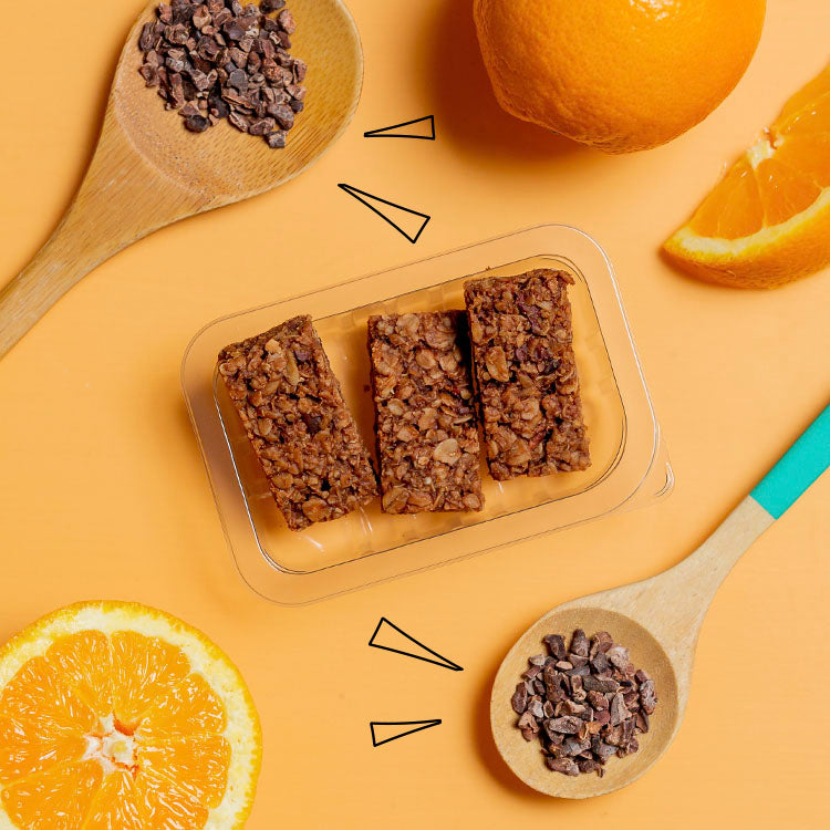 cocoa orange flapjack in a punnet with slices of orange and cacao nibs scattered around it
